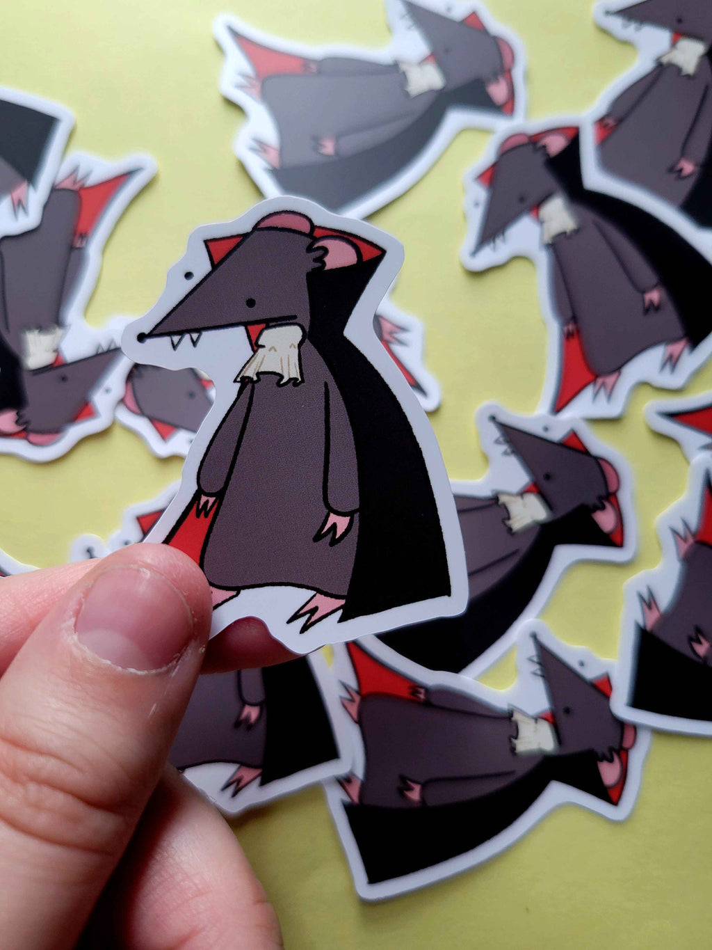 a picture of a hand holding a sticker of a rat in a dracula costume